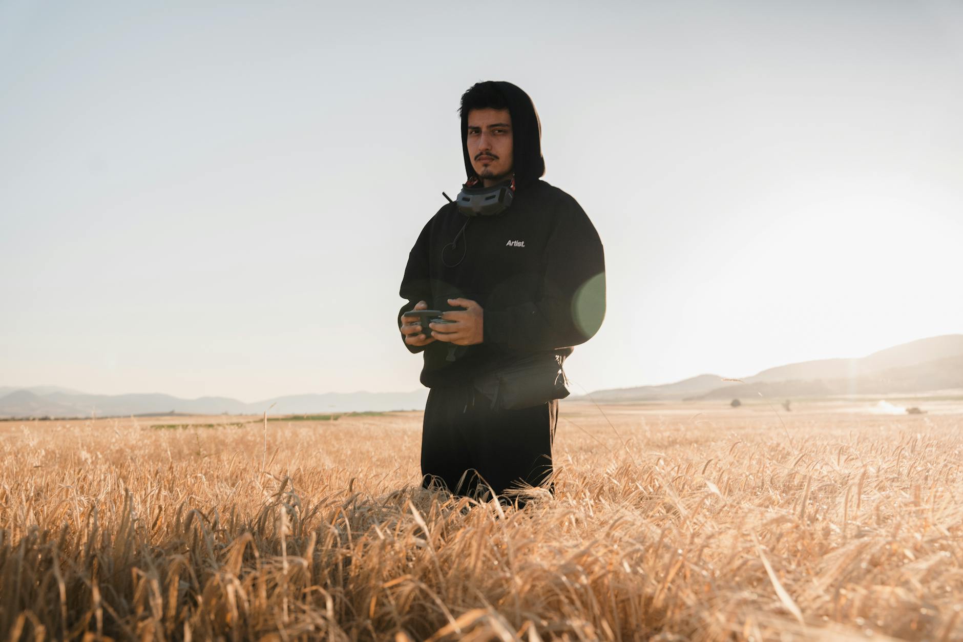 Young man operating a drone in a golden wheat field during the day.