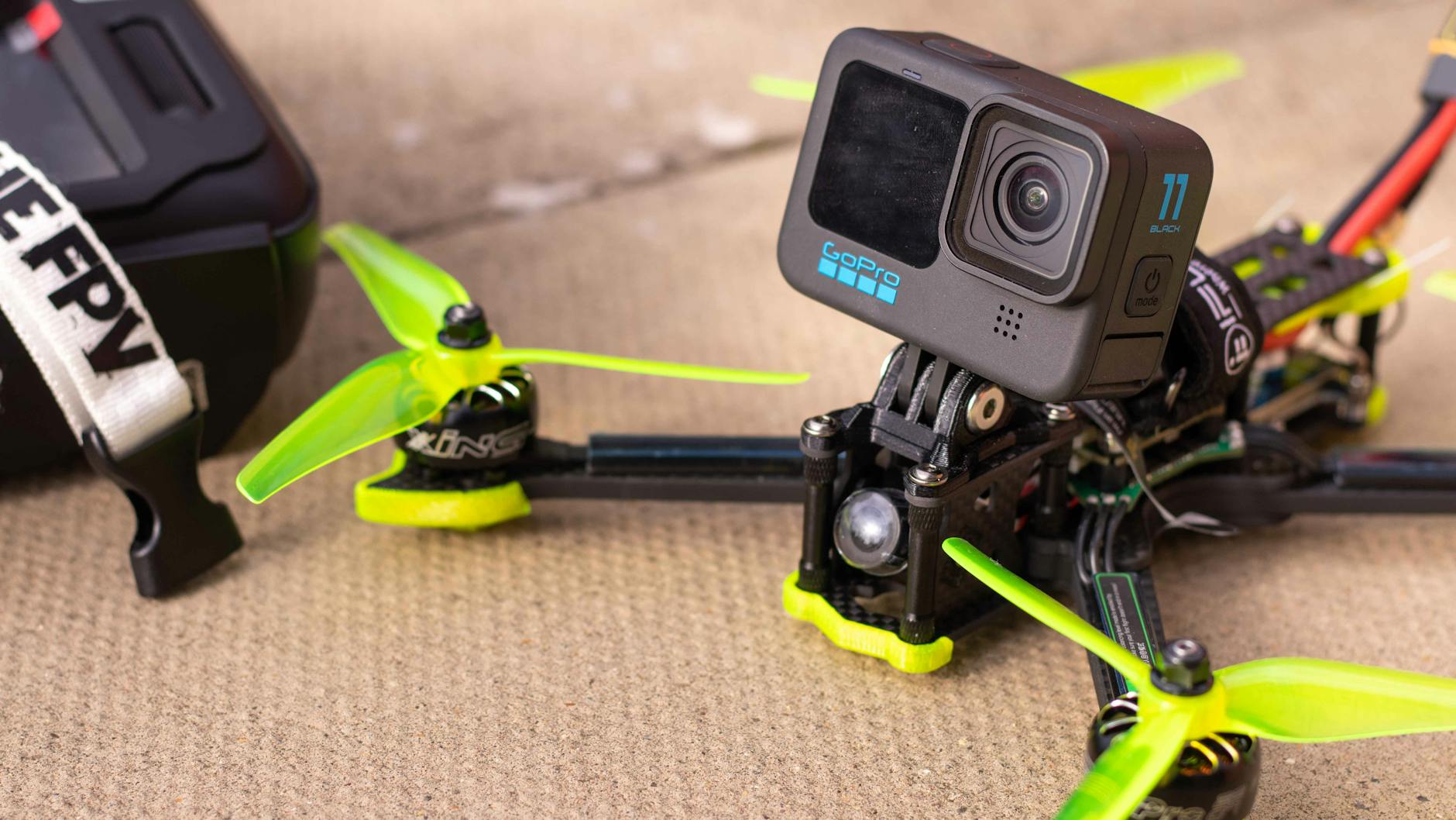 Close-up of a FPV drone equipped with an action camera on a textured surface.