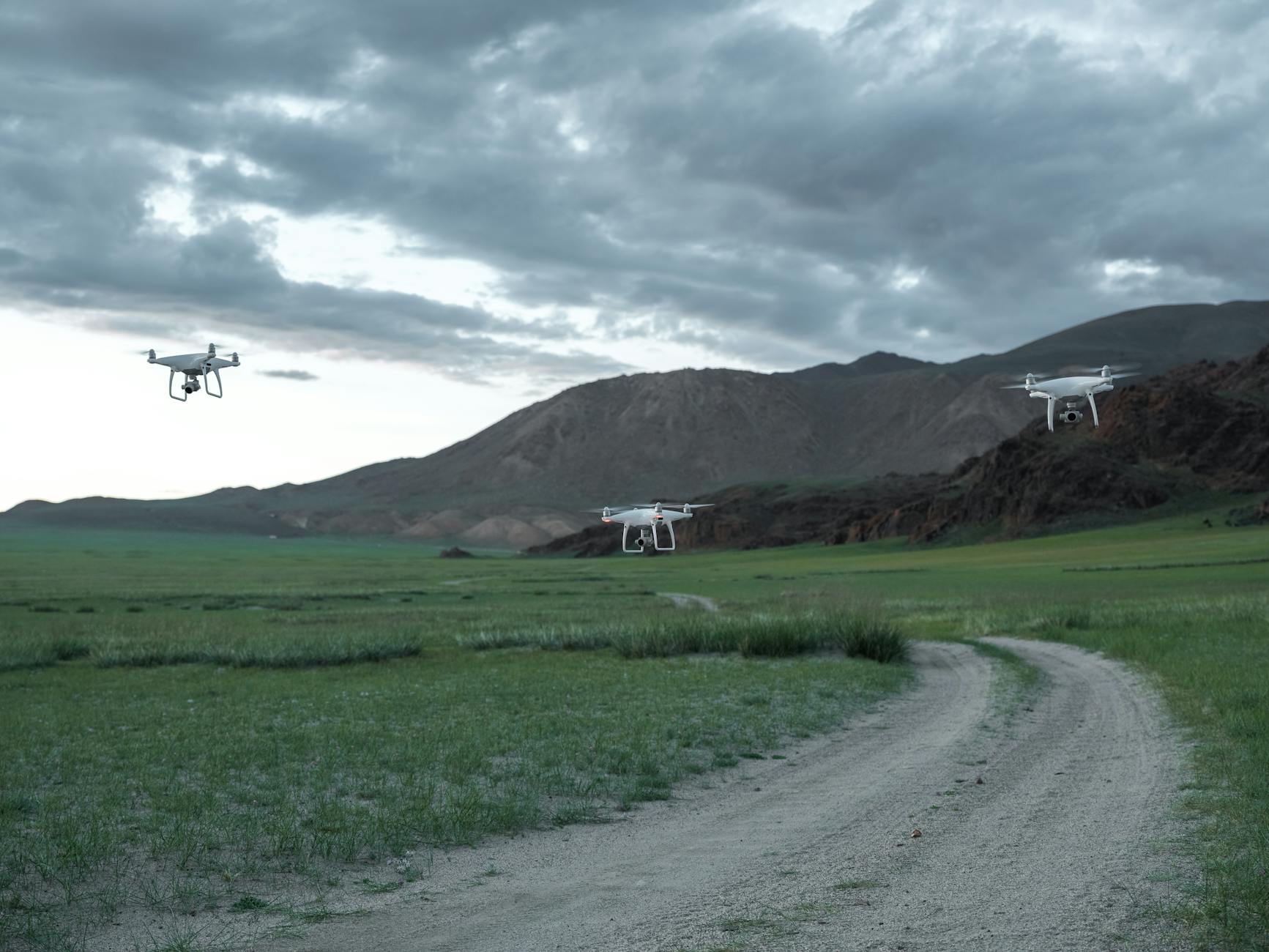 Aerial drones hovering over a picturesque landscape with fields and mountains under a cloudy sky.