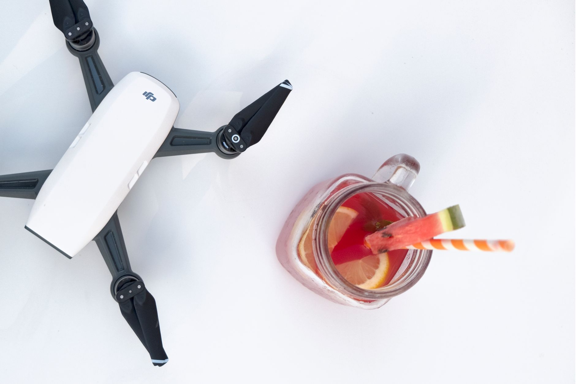 A top-down view of a drone and a refreshing fruit drink with lemon slices and a straw, set against a minimalist background.
