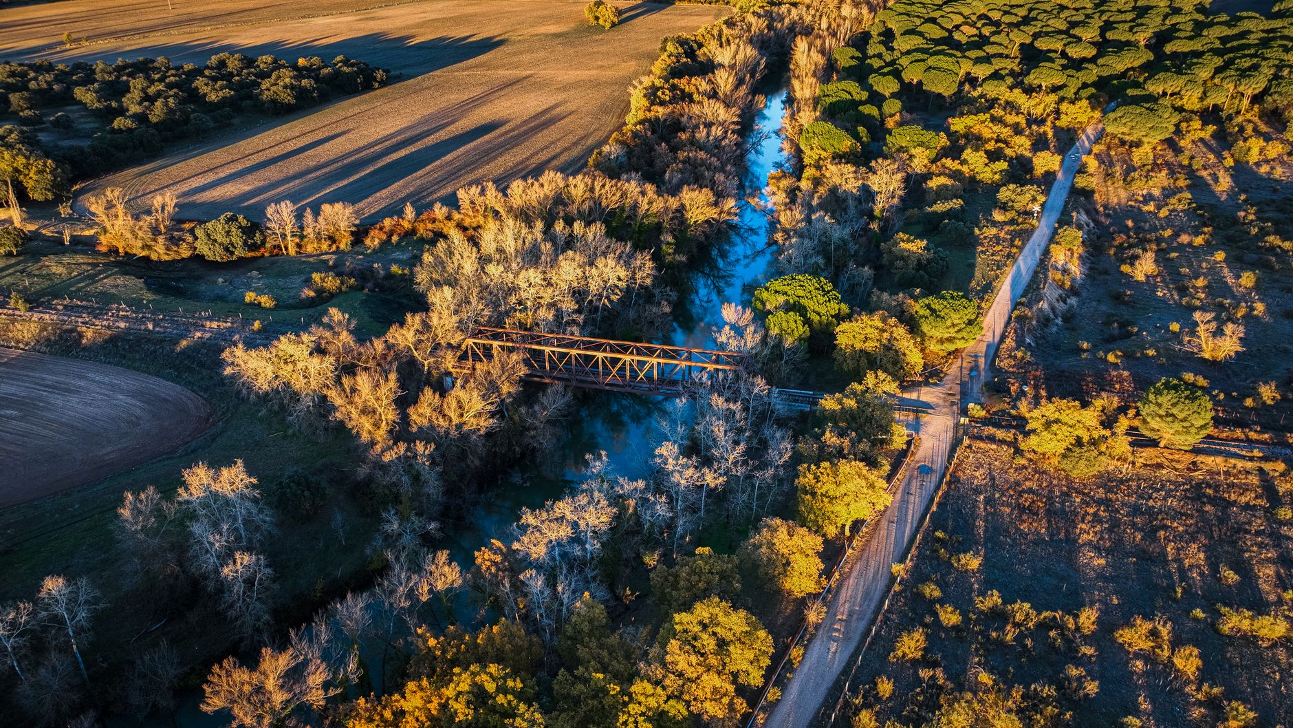 Stunning aerial view of an iron bridge over a river surrounded by lush fields in Valladolid at sunset.