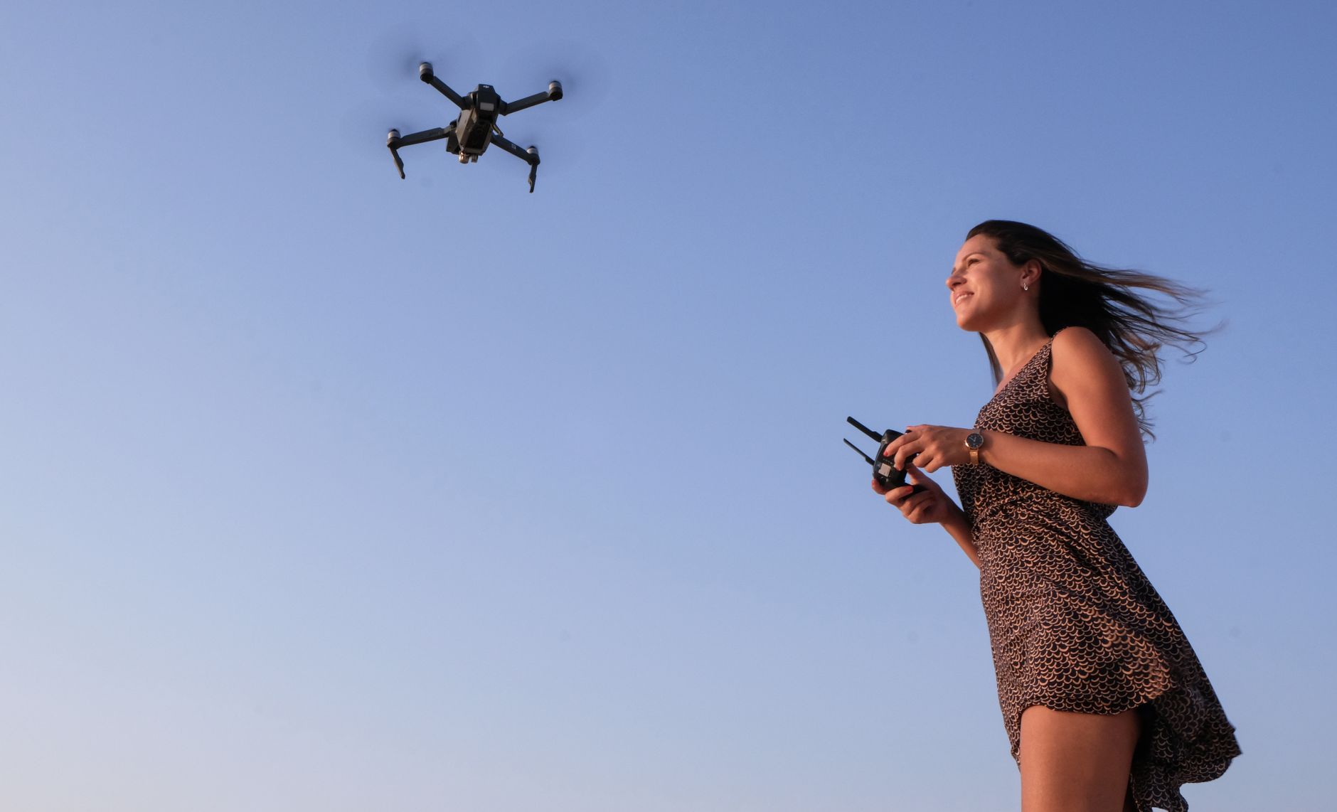 A woman enjoying flying a drone outdoors under a clear blue sky.