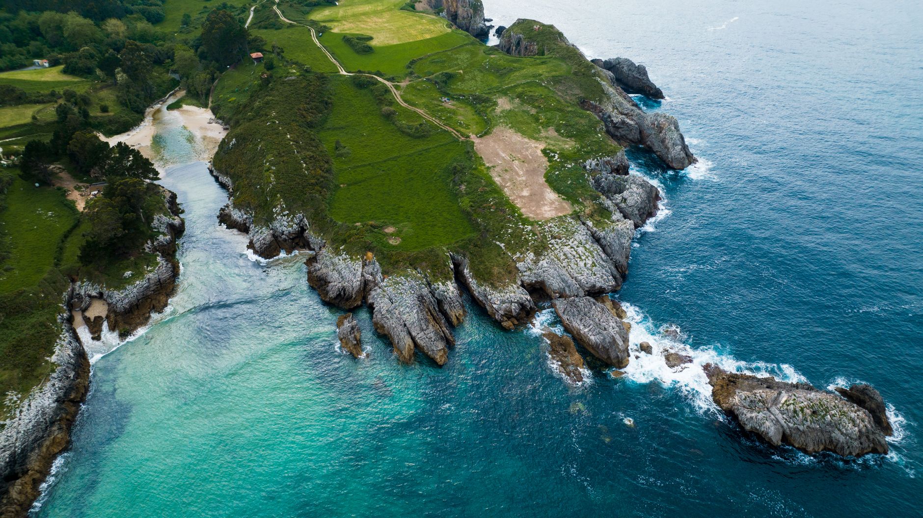 Aerial shot of the stunning rocky coastline in Northern Spain, featuring lush greenery and blue ocean waters.